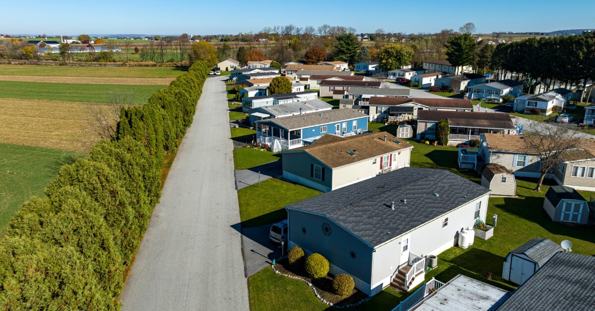 An aerial view shows a community of mobile homes. They are surrounded by farm fields and mature trees.