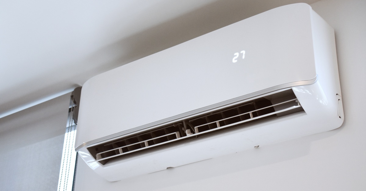 A white mini split air conditioning system is mounted on a white wall next to a window. The number 27 is on the split system.