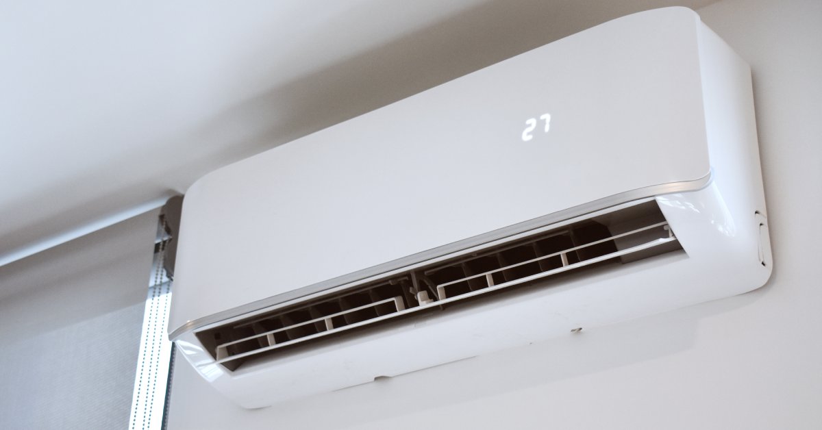 A close-up view shows a white, ductless air conditioning unit attached to the white wall of a home.