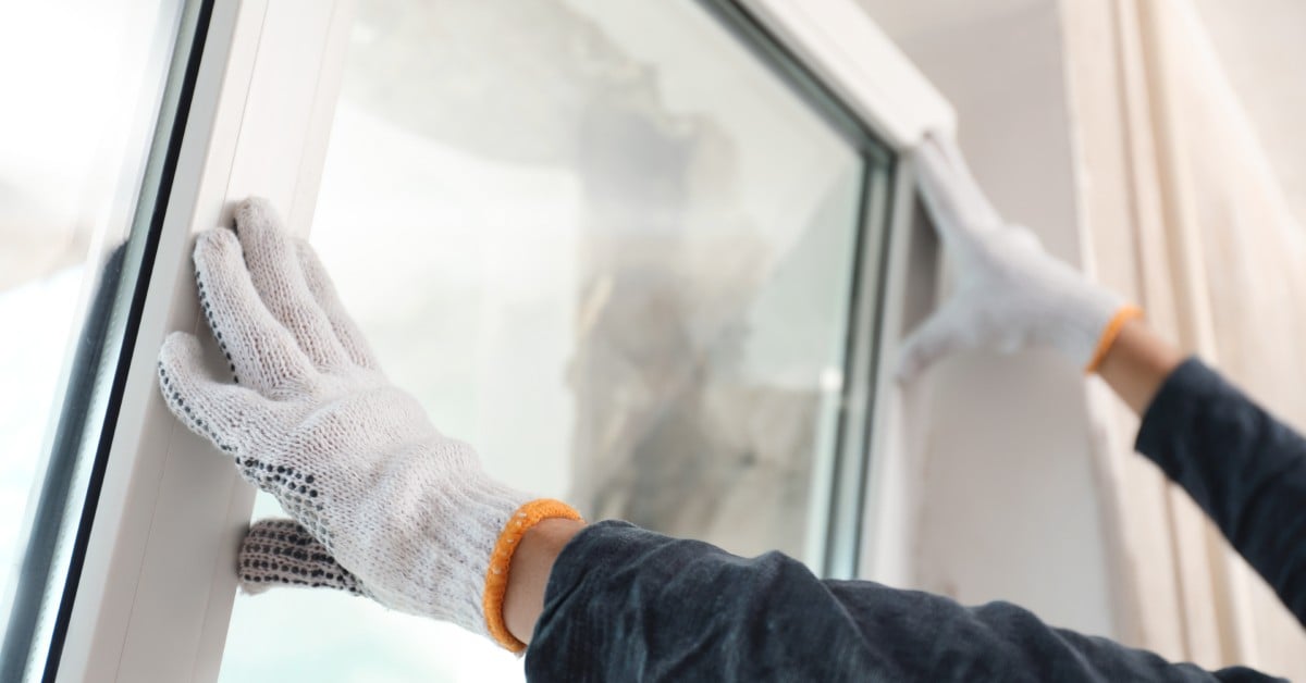 A close-up view shows a person wearing white working gloves and a black shirt installing a window.
