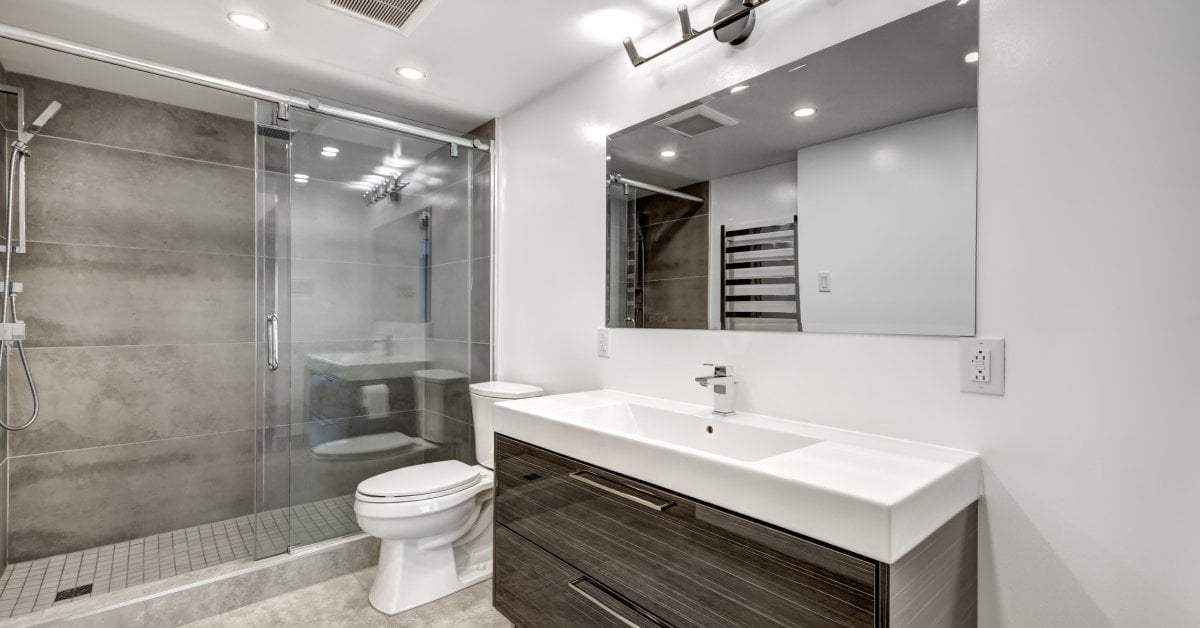 A modern bathroom features a walk-in shower with sliding glass doors, a white toilet, and a wooden vanity with a white sink.