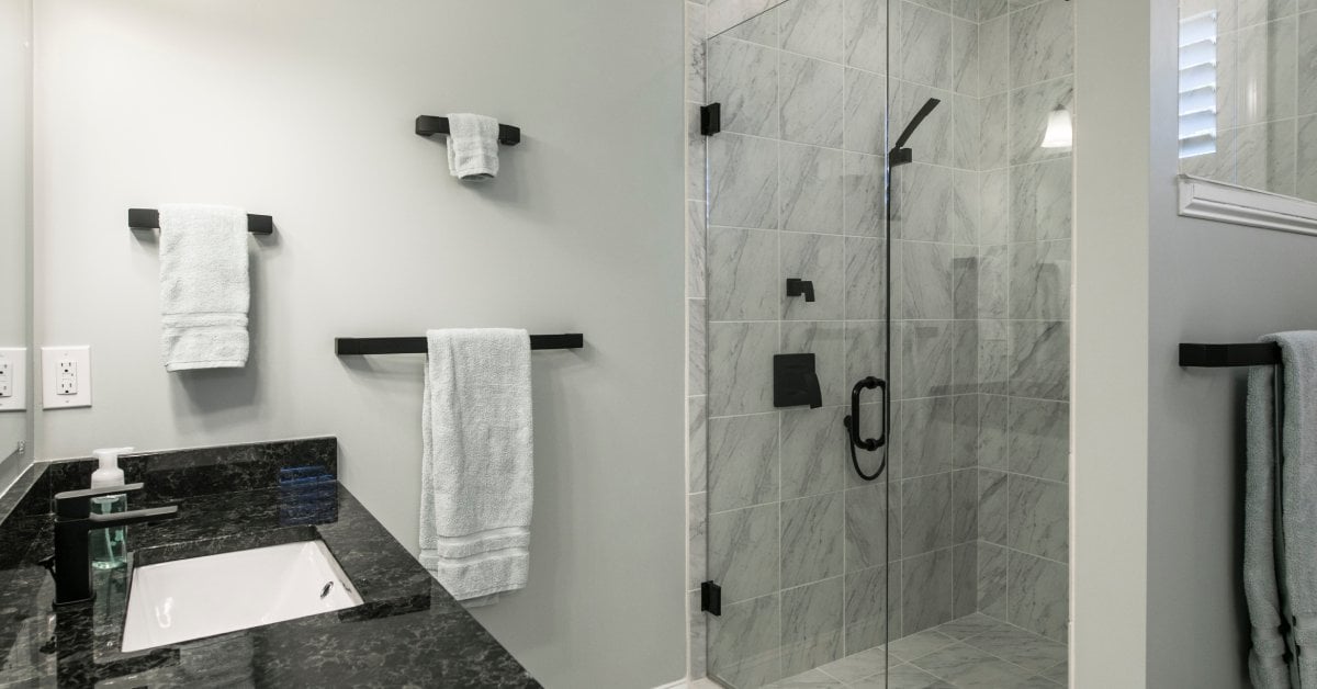 A bathroom features a sink with black countertops, a walk-in shower, black fixtures, and a gray-tiled floor.