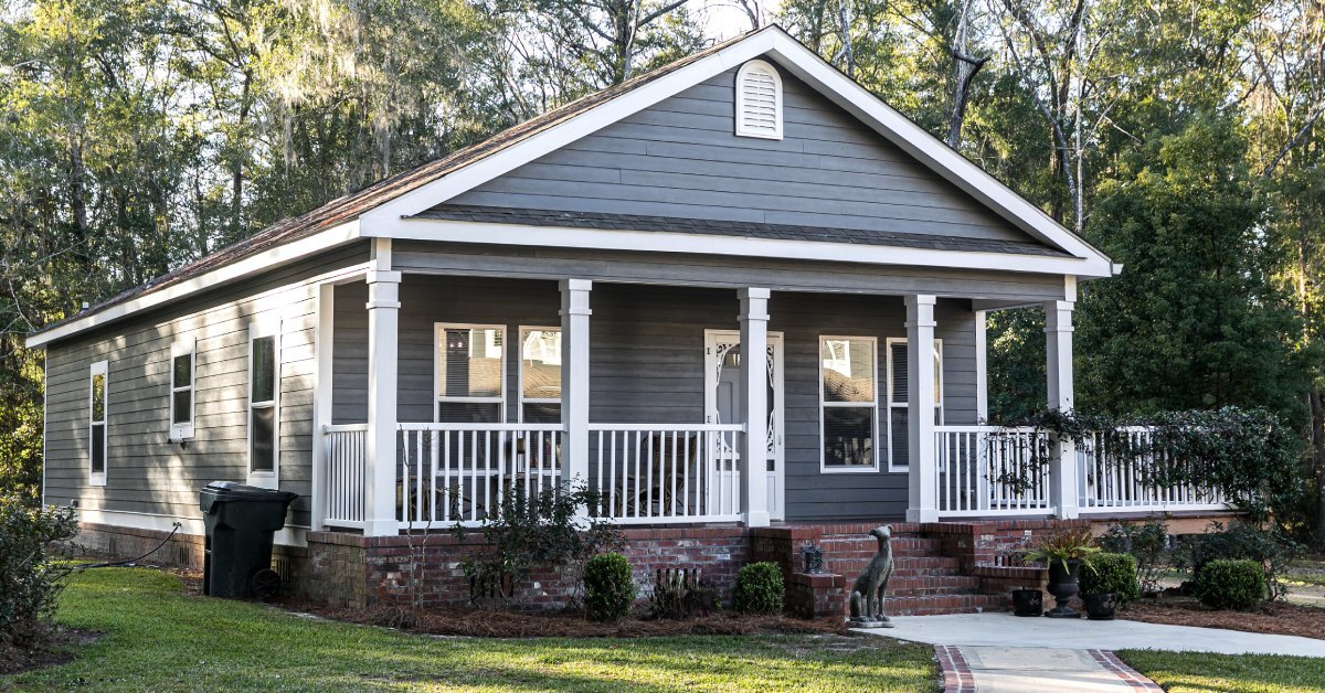 A manufactured home features gray siding and red brick around its base. It also has a brick front porch.