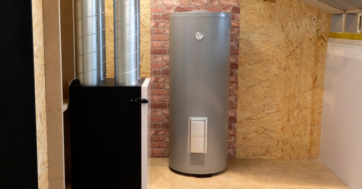 A large gray water tank sits alone in an unfinished room that as ply-wood on the floors and a partial brick wall.