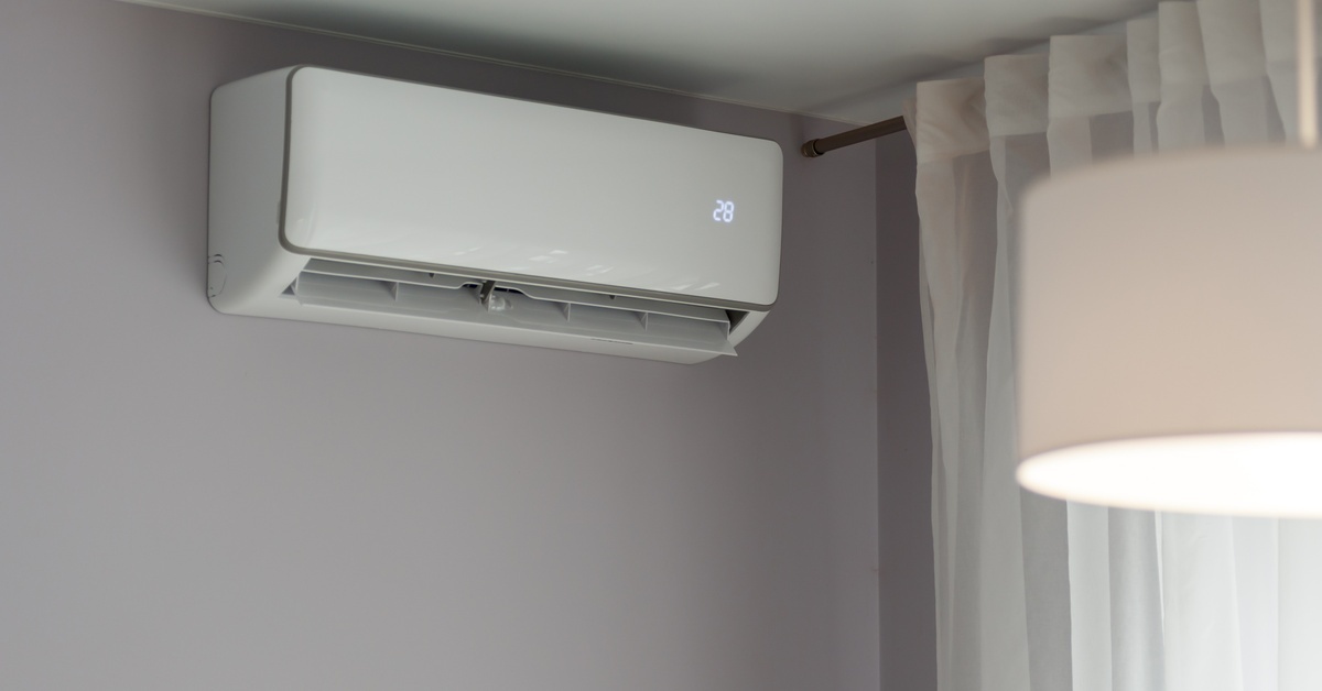 A white split system AC unit mounted to a gray wall near the ceiling. The number 28 glows on the front of the AC unit.