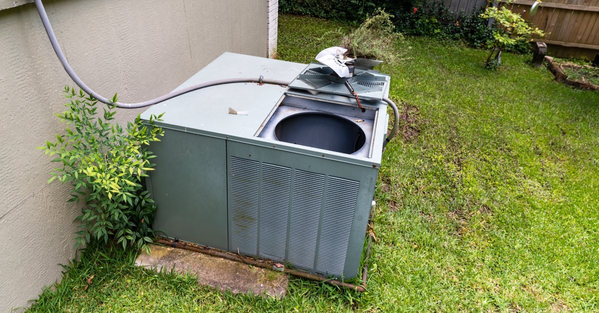 An open packaged air conditioning system sitting in the grass beside a home. A hose connects the AC unit to the house.