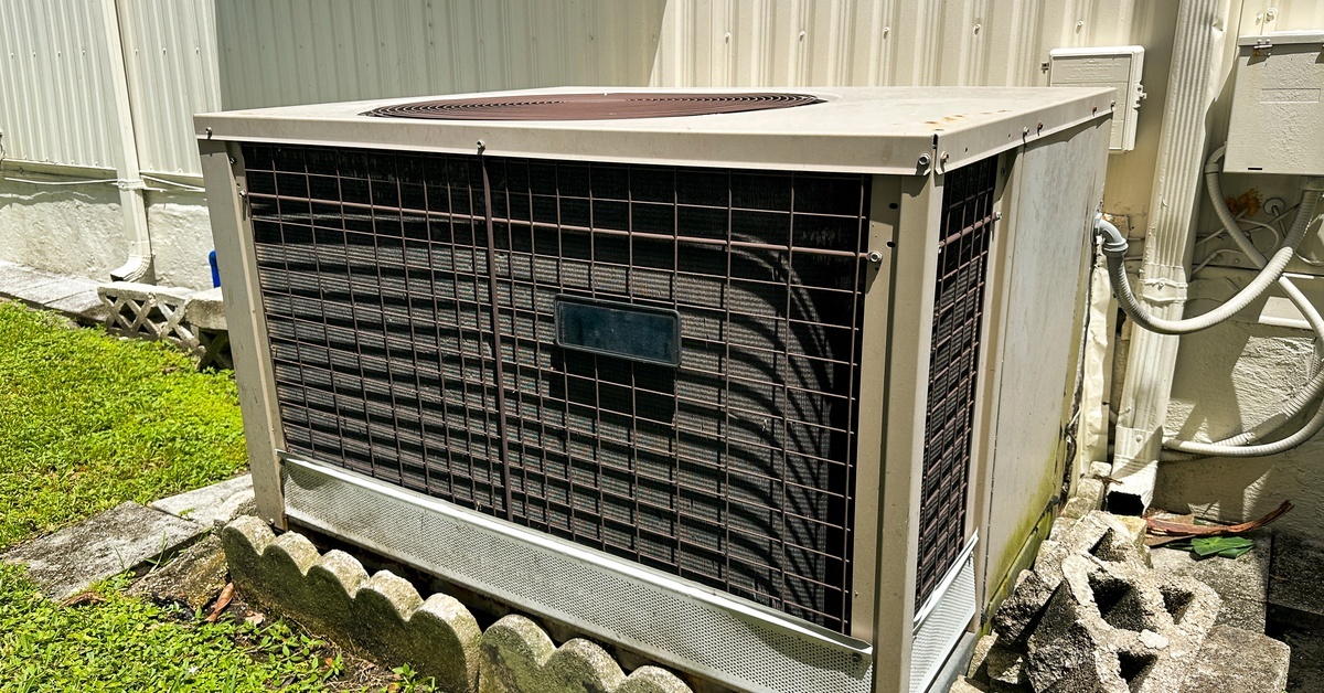 A large HVAC system on the outside of a cream-colored home. Small stones and grass surround the HVAC unit.