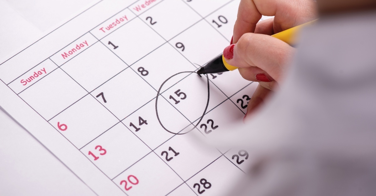 A hand uses a black marker to draw a big circle around the 15th day of a blank monthly calendar print-out.