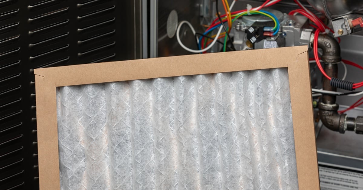 A new fiberglass furnace filter sits near an HVAC unit. The open HVAC unit reveals colorful wires and metal tubing.