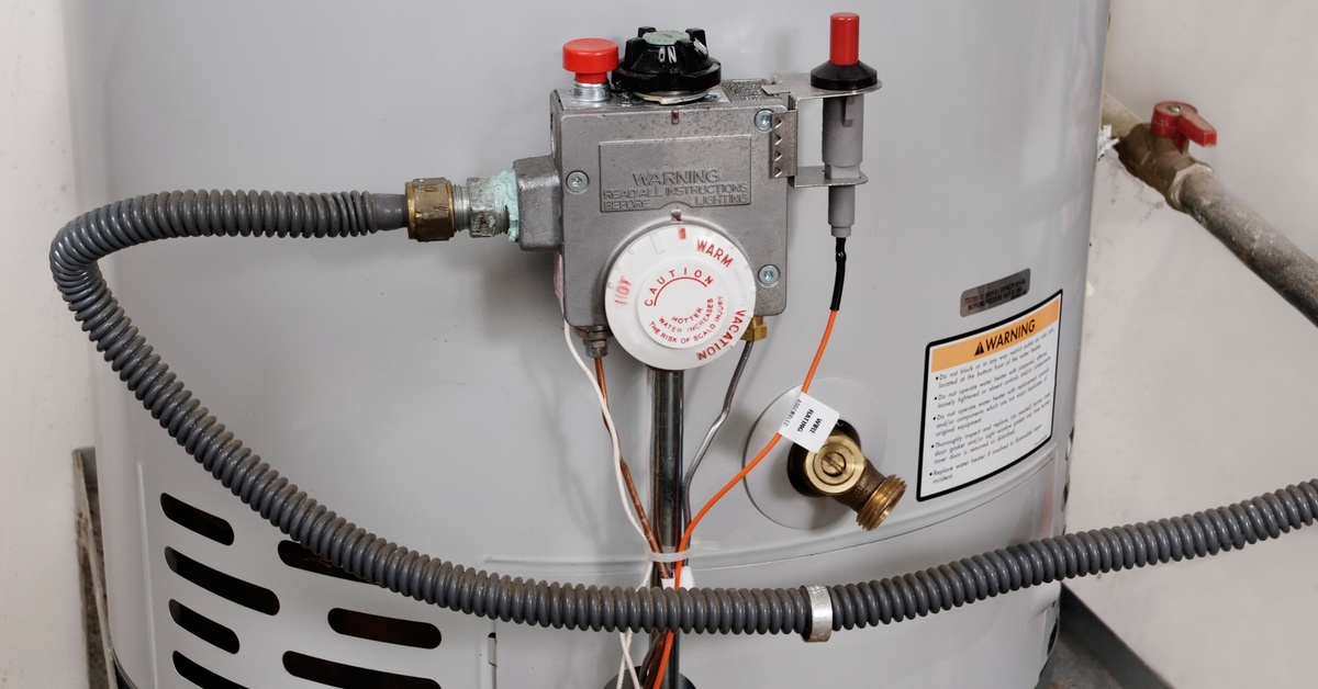 A close-up view of a white water temperature dial and the gas supply line on a gas hot water heater.