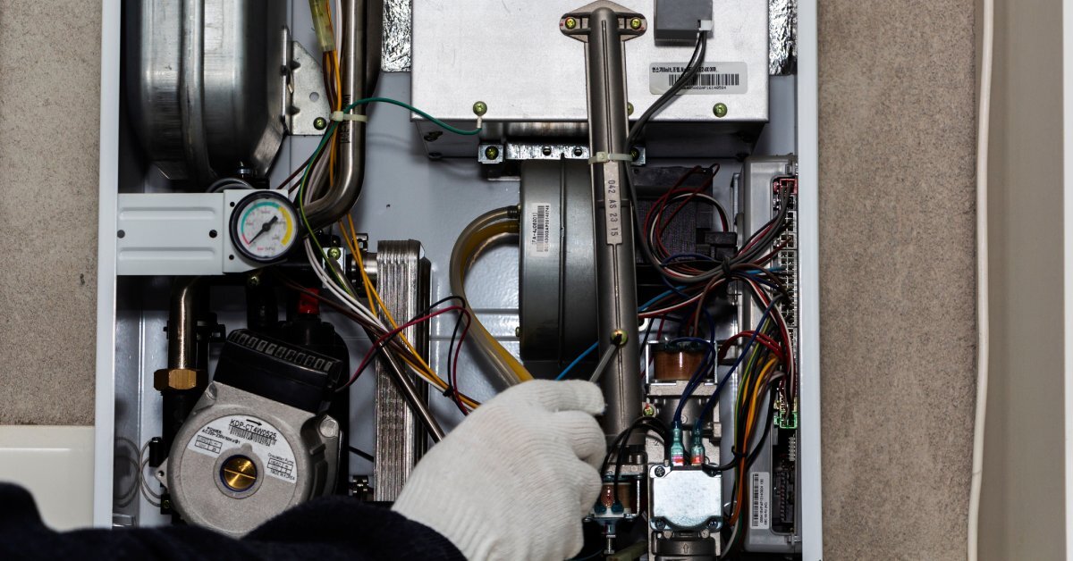 A technician's white gloved hand uses a screwdriver to make an adjustment to the inside of a residential furnace.