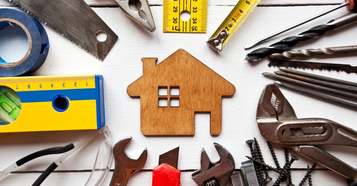 A selection of tools such as a wrench, level, saw, and screwdriver are arranged in a circle around a wooden house model.